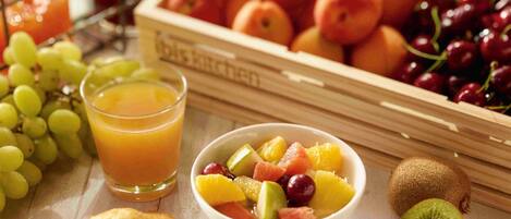 Un cuenco de frutas con uvas, kiwi y otras frutas, un vaso de jugo de naranja y una caja de melocotones.