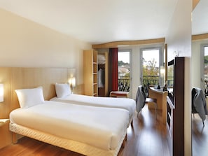 Habitación de hotel con dos camas, un escritorio, una silla, un armario y un balcón con vistas.