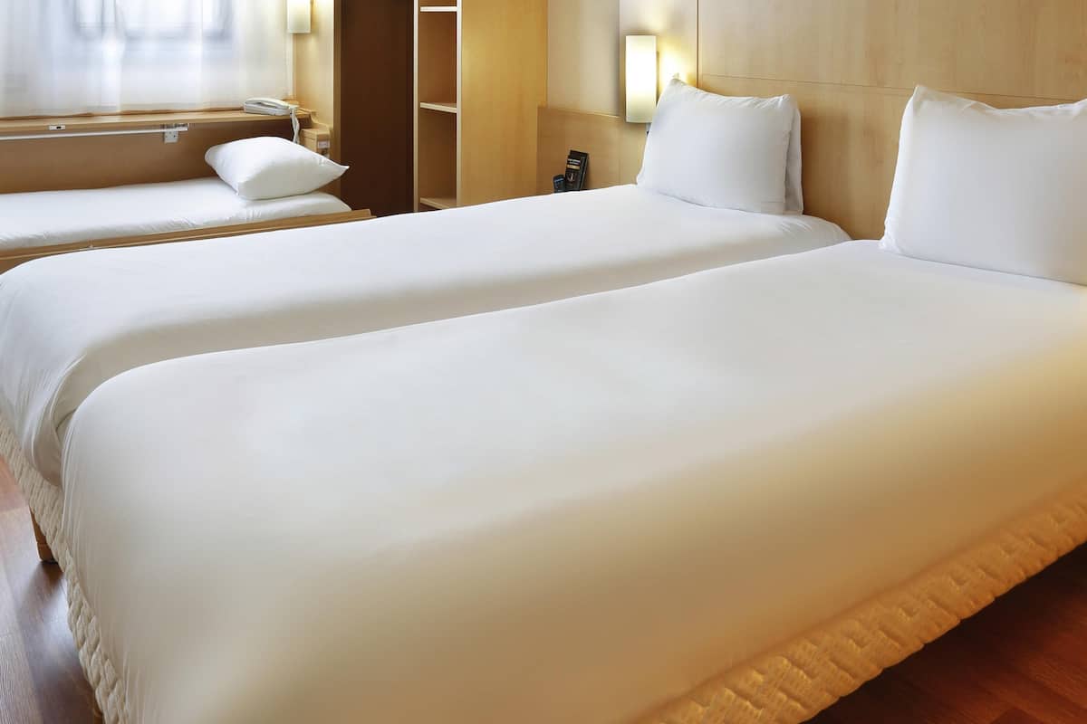 A hotel room with two beds, a bedside table, a lamp, and a wardrobe.
