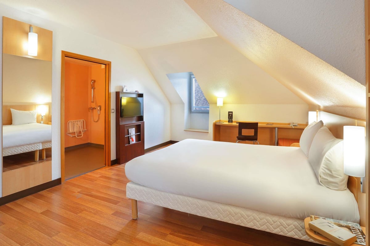 A modern hotel room with a large bed, a desk, a TV, and a shower.