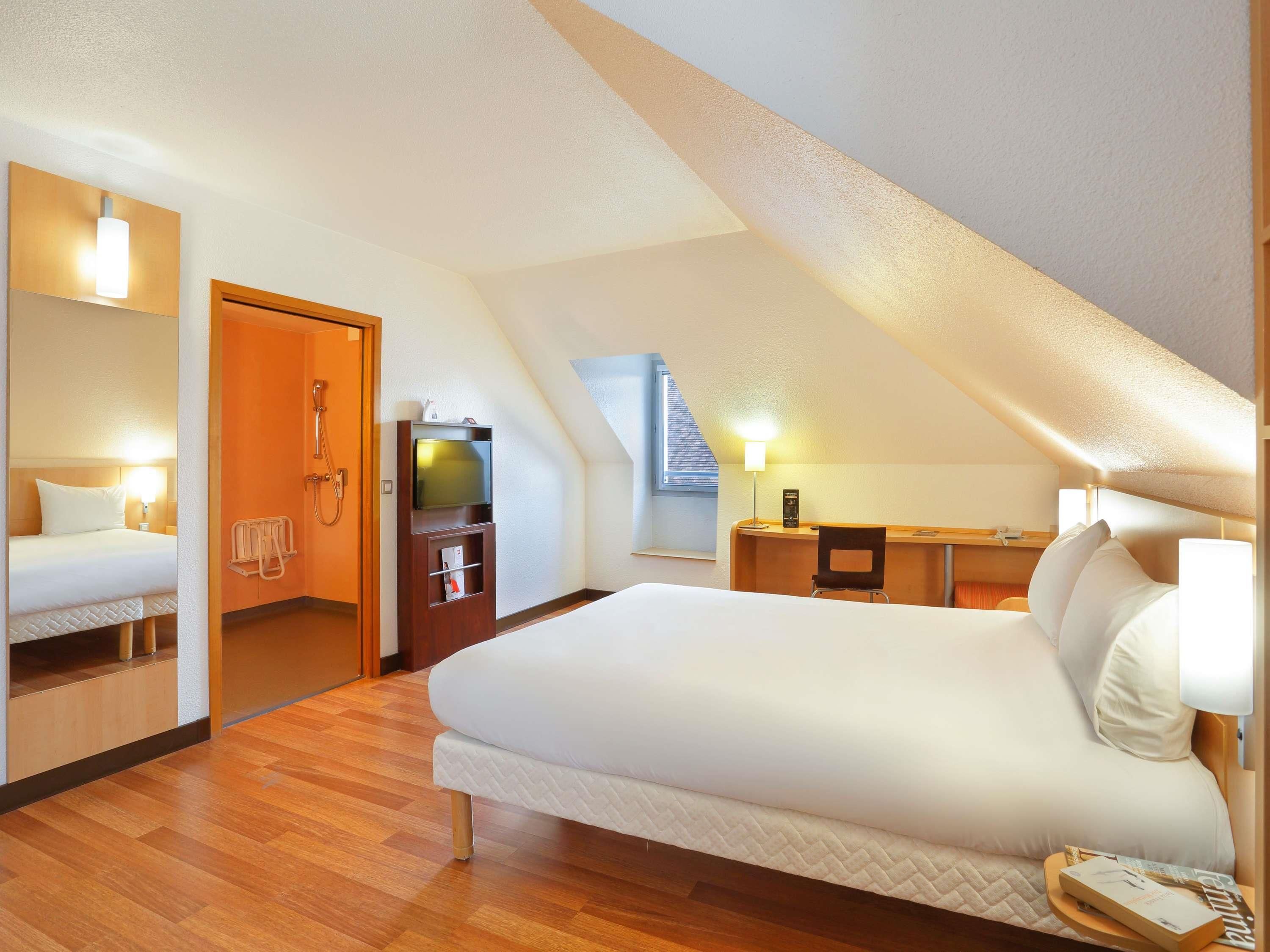 Ett modernt hotellrum med en stor säng, ett skrivbord, en TV och en dusch.