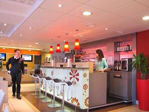 A modern bar area with a counter, bar stools, and a woman standing behind the counter. - ibis Etampes (Etampes)