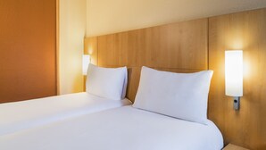A neatly made bed with white linens, a wooden headboard, and two wall-mounted bedside lamps. - ibis Etampes (Etampes)