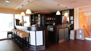 A bar area with a counter, stools, and hanging lights. There are shelves with bottles and glasses behind the counter. - Hotels & Appartments Feuerschiff (3114375) (Langeoog)
