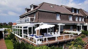 A two-story house with a covered patio area featuring lounge chairs and umbrellas. - Hotels & Appartments Feuerschiff (3114375) (Langeoog)