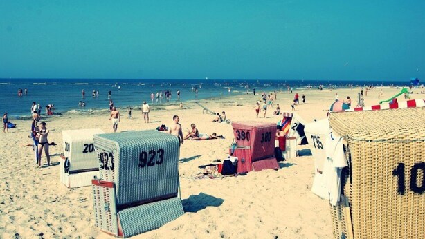A beach with numbered beach chairs and umbrellas, a clear sky, and people enjoying the beach. - Hotels & Appartments Feuerschiff (3114375) (Langeoog)