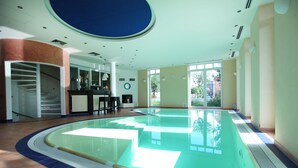 An indoor swimming pool with a clear view of the outside through large windows, a staircase, and a reception area. - Hotels & Appartments Feuerschiff (3114375) (Langeoog)