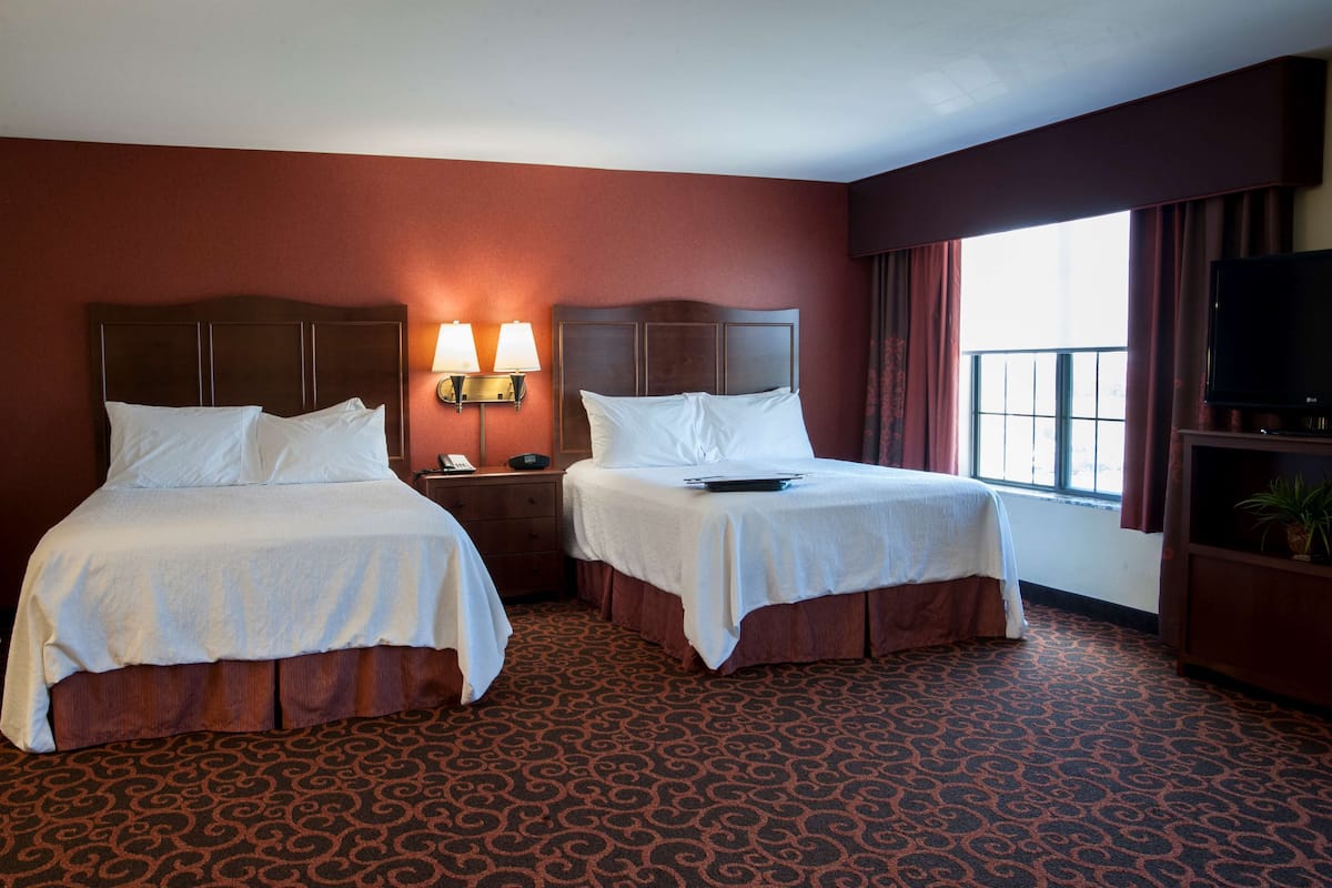 A hotel room with two beds, a TV, a nightstand, and a window with curtains.
