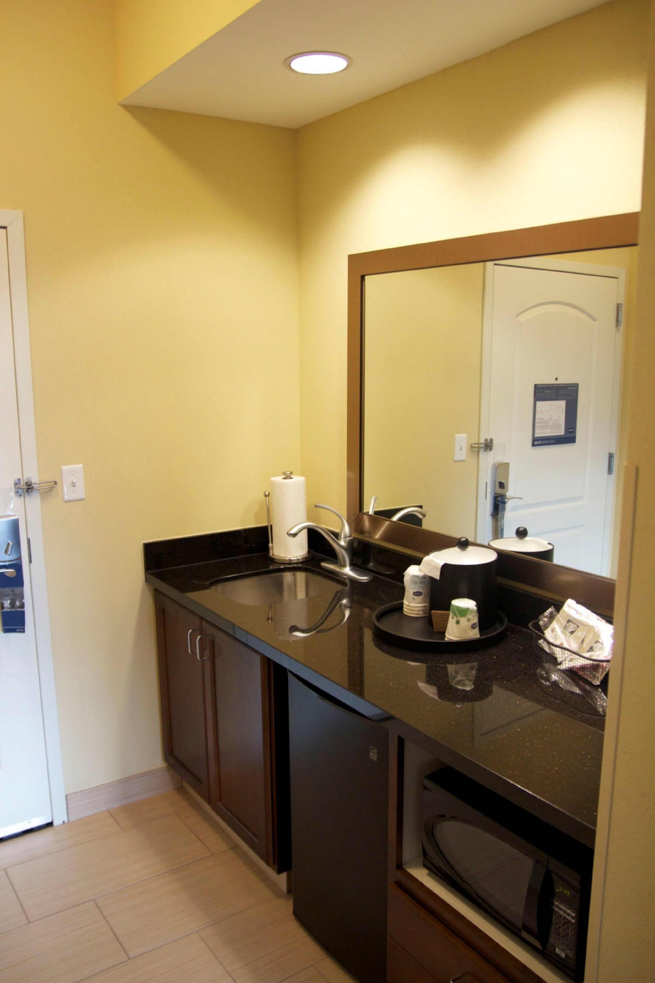 A compact bathroom with a sink, mirror, and a microwave.