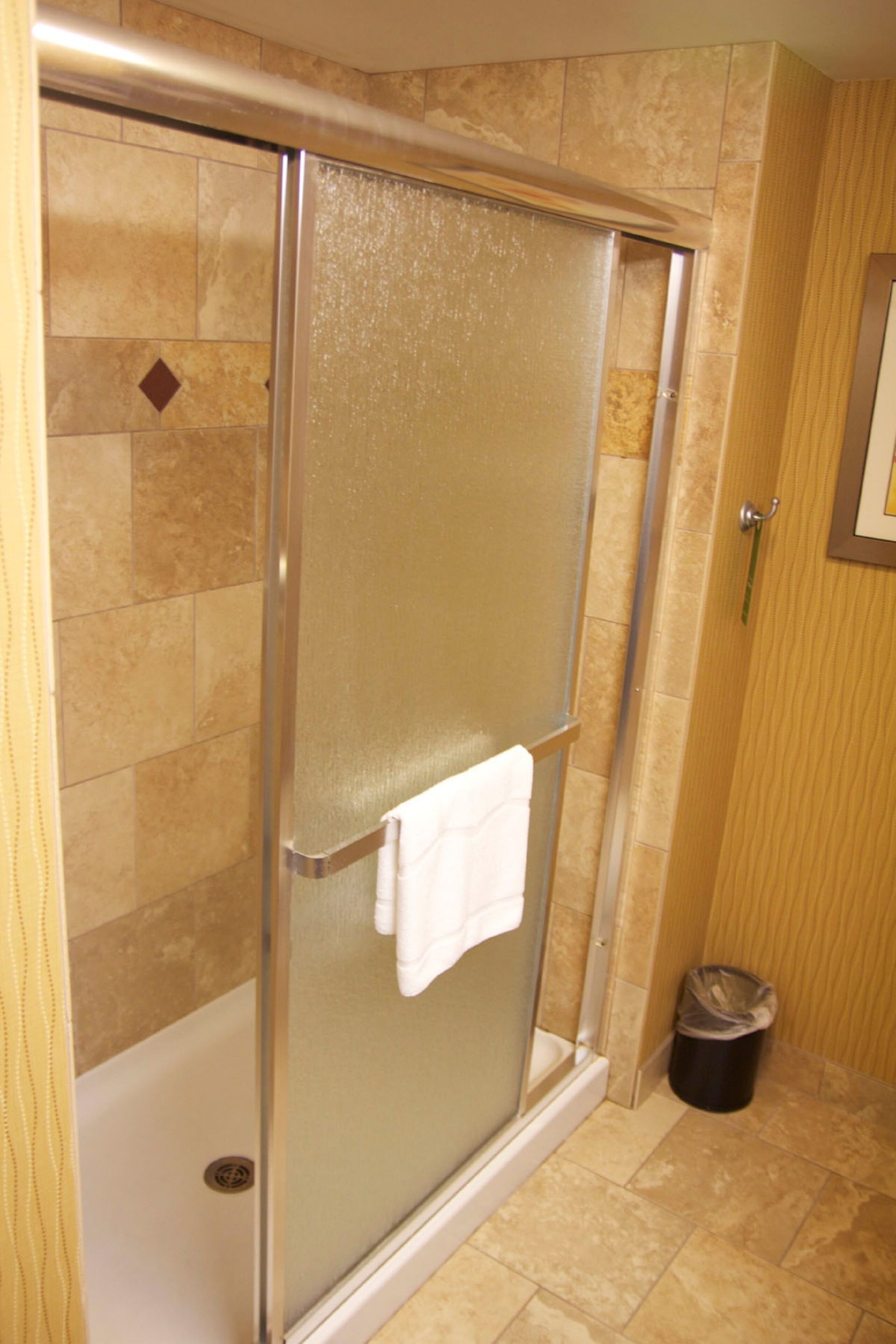 Une cabine de douche fermée par des parois en verre, avec une serviette blanche accrochée à la porte.