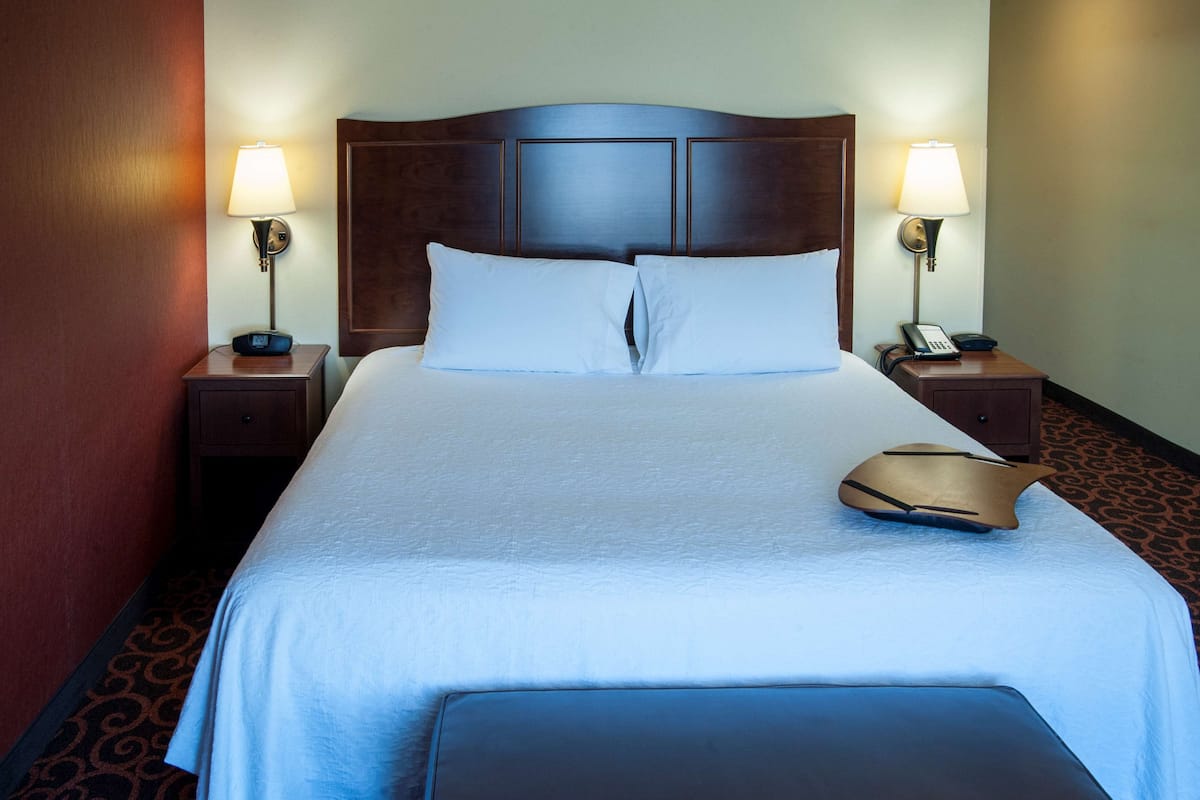 A neatly made bed with white linens, two bedside lamps, a telephone, and a bedside table.
