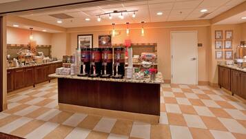 A hotel lobby with a checkered floor, a central counter with beverage dispensers, and a door in the background.