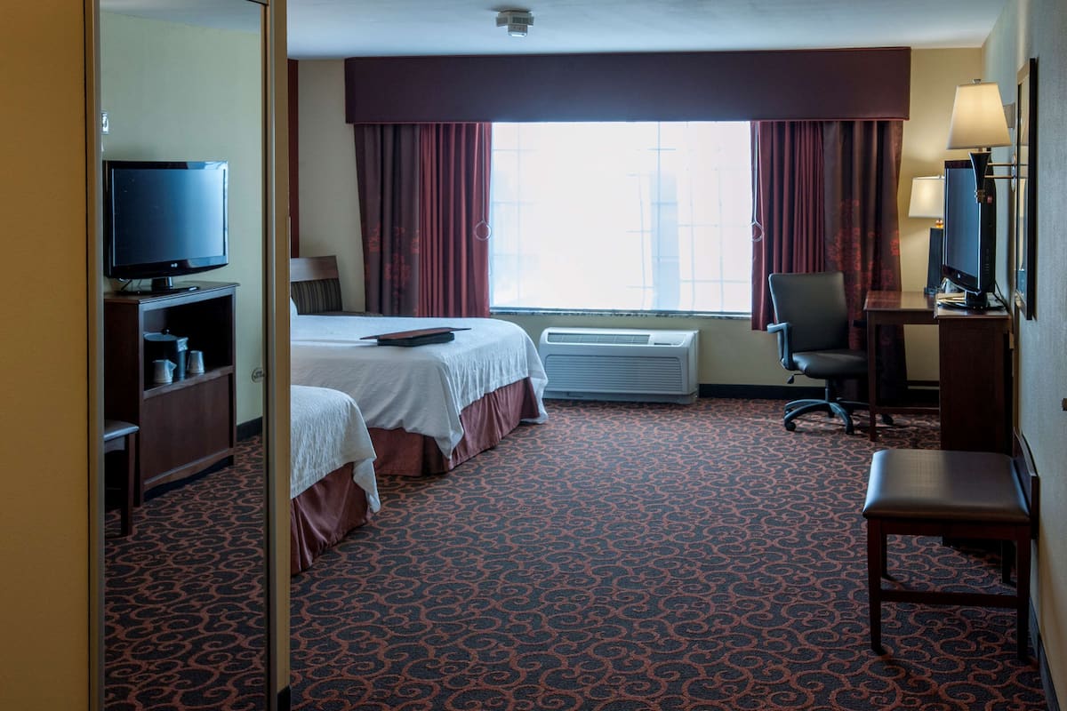 A hotel room with two beds, a desk with a chair, a television, and an air conditioning unit.