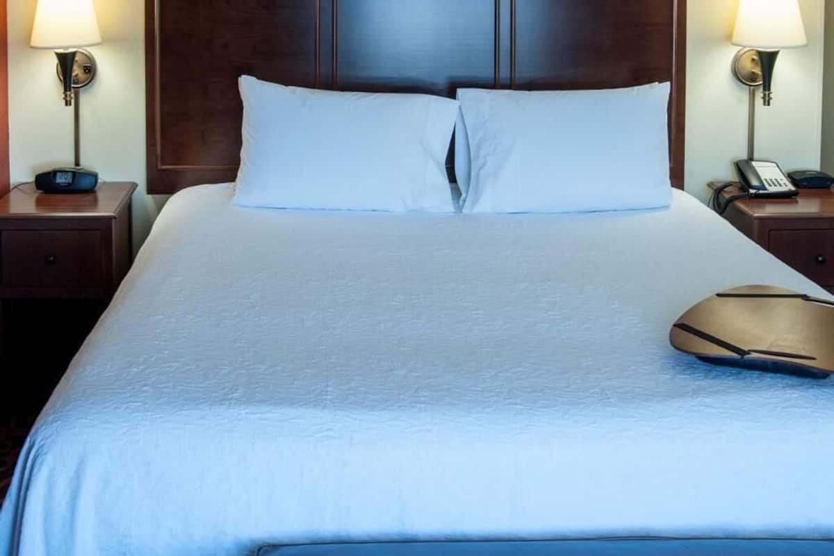 A neatly made bed with white linens, two bedside lamps, and a bedside phone on a wooden nightstand.