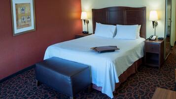 A hotel room with a large bed, two bedside tables with lamps, a small bench, and a carpeted floor.