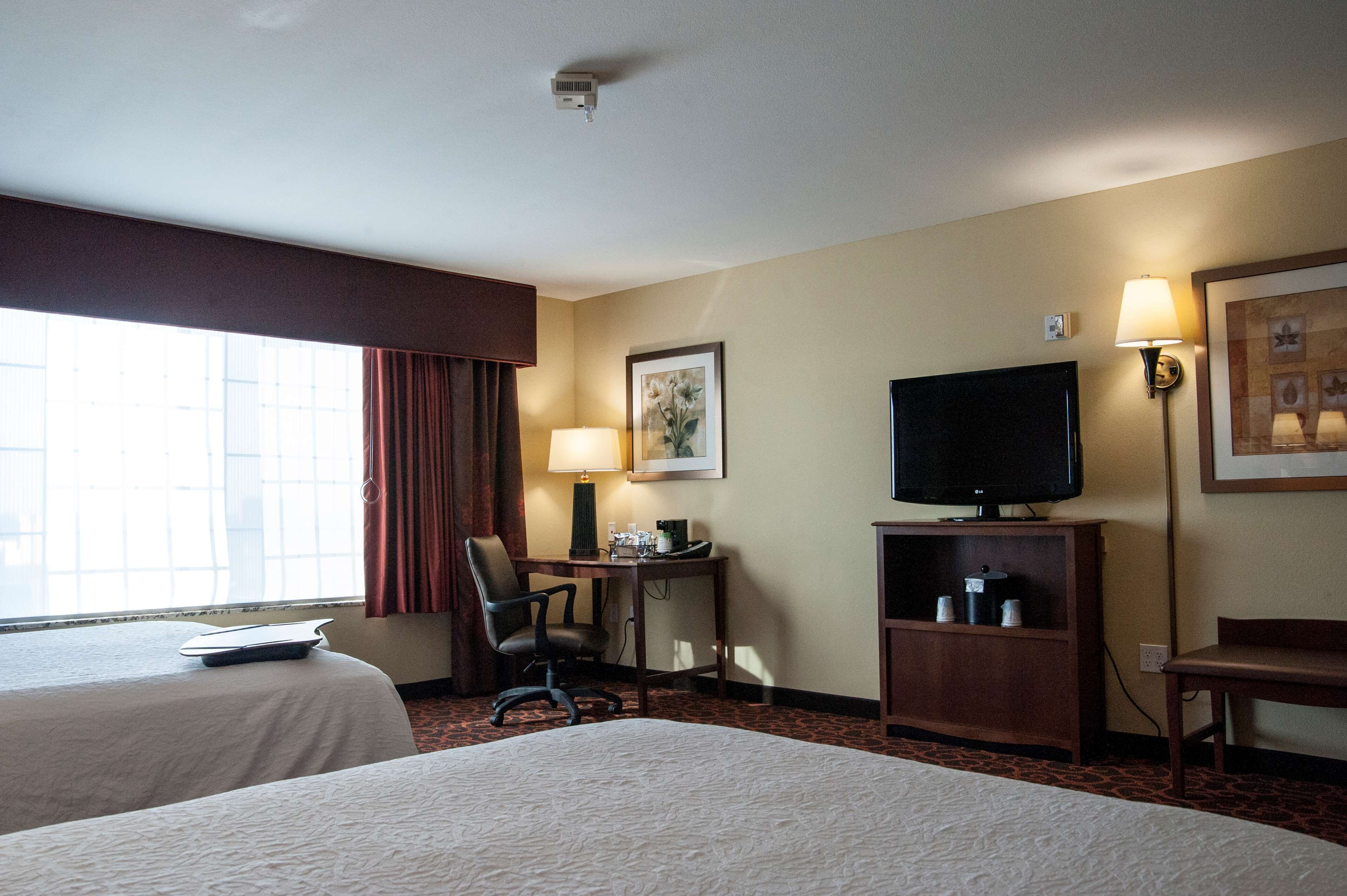 A hotel room with two beds, a desk with a lamp, a television, and a window with curtains.