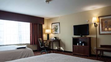 A hotel room with two beds, a desk with a lamp, a television, and a window with curtains.