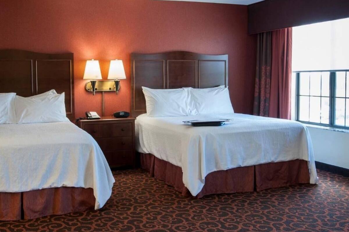 A hotel room with two beds, a nightstand with lamps, and a window with curtains.