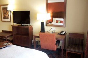 Habitación de hotel con cama, escritorio con lámpara, televisión, silla y teléfono.