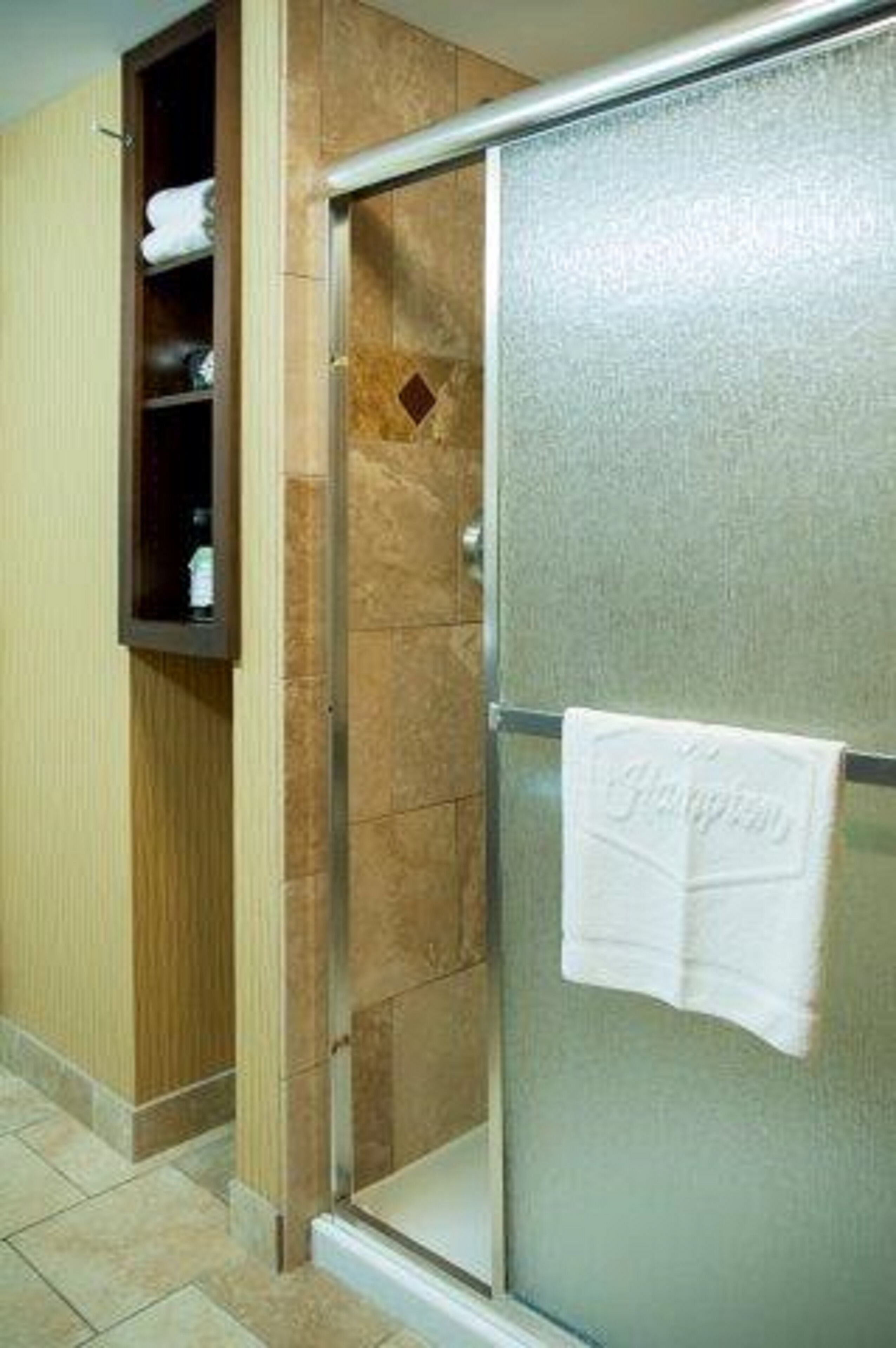 A bathroom with a glass shower enclosure, a wooden cabinet, and a towel hanging on the glass door.