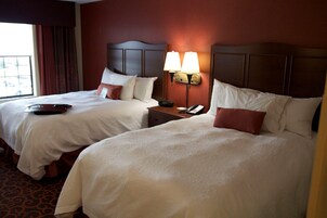 Habitación de hotel con dos camas, una mesita de noche con lámpara y una ventana con cortinas.