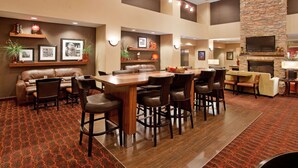 A spacious lobby with a long wooden table, leather seating, and a stone fireplace.