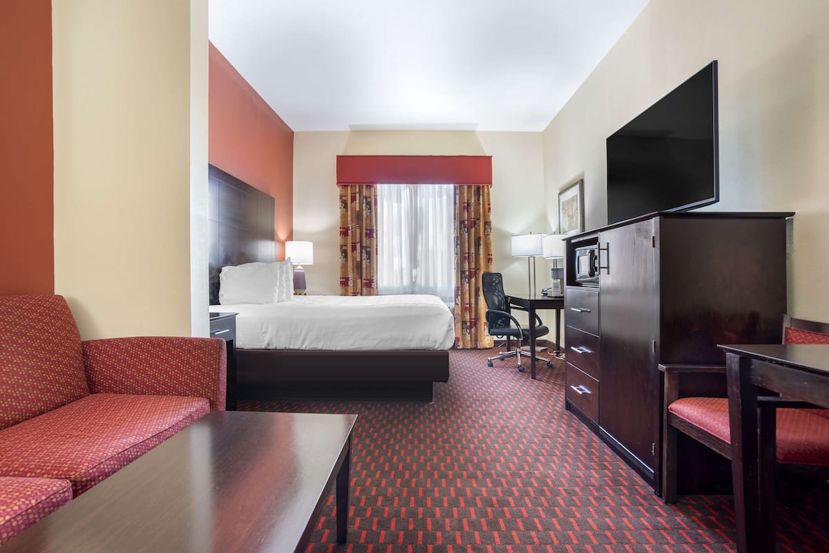 Ein Hotelzimmer mit Bett, Schreibtisch, Sessel, Fernseher und einer Couch.