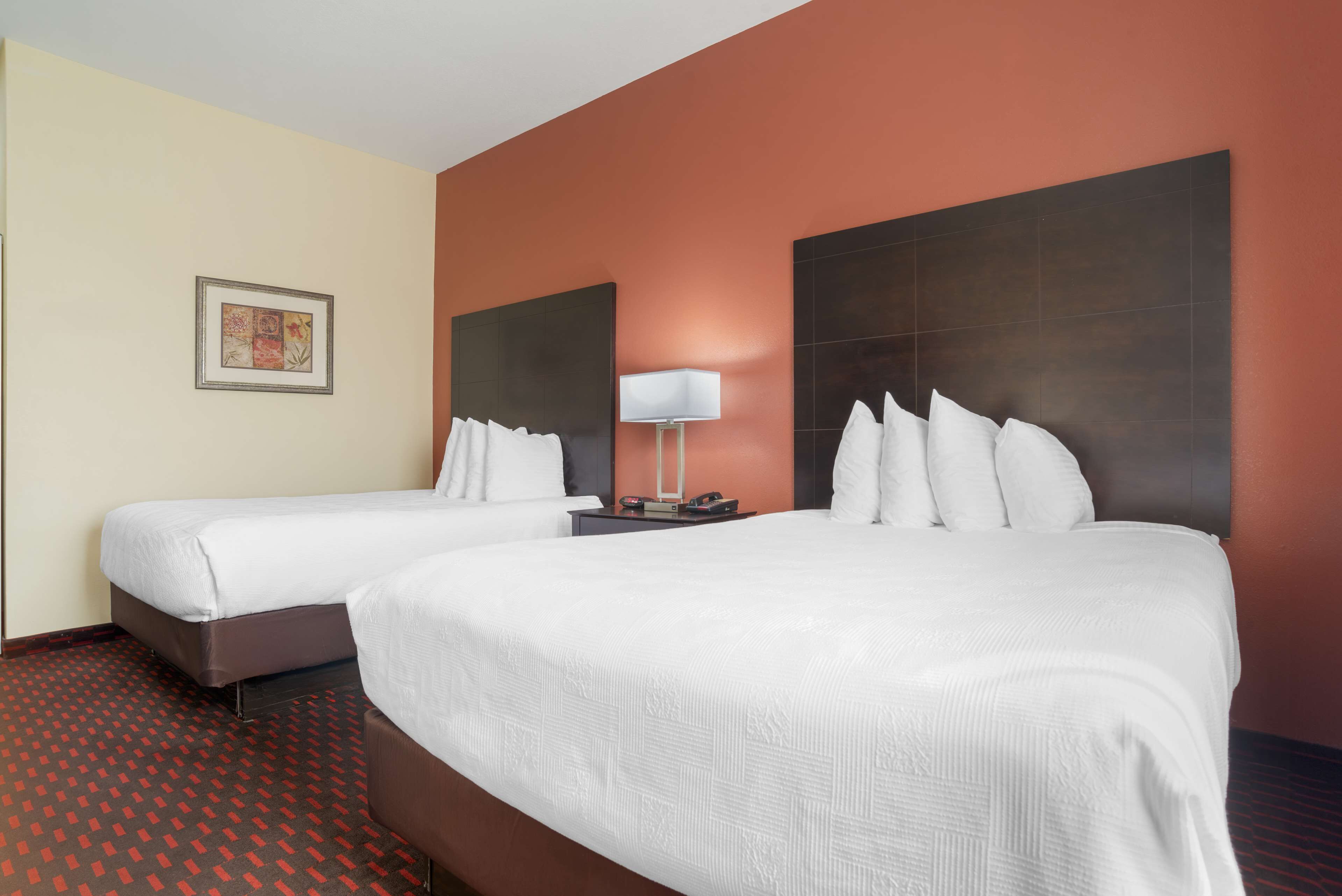 A hotel room with two beds, a nightstand with a lamp, and a framed picture on the wall.