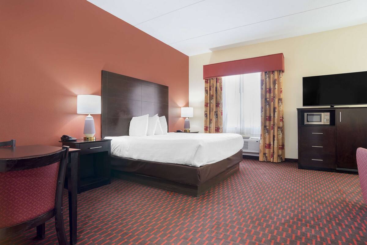 Ein Hotelzimmer mit einem Bett, zwei Nachttischen mit Lampen, einem Schreibtisch mit Stuhl, einem Fernseher und einer Mikrowelle.