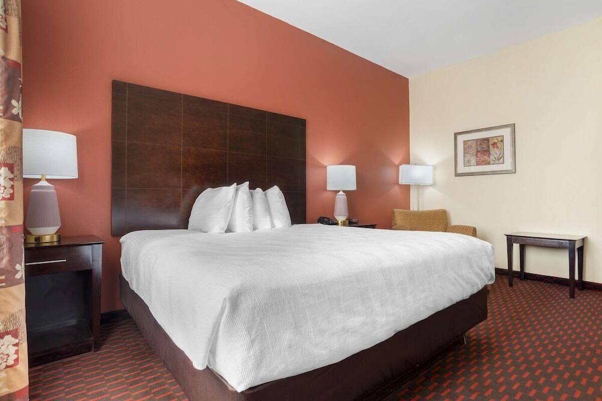 Habitación de hotel con una cama grande, dos lámparas de noche, una mesita y un cuadro colgado en la pared.
