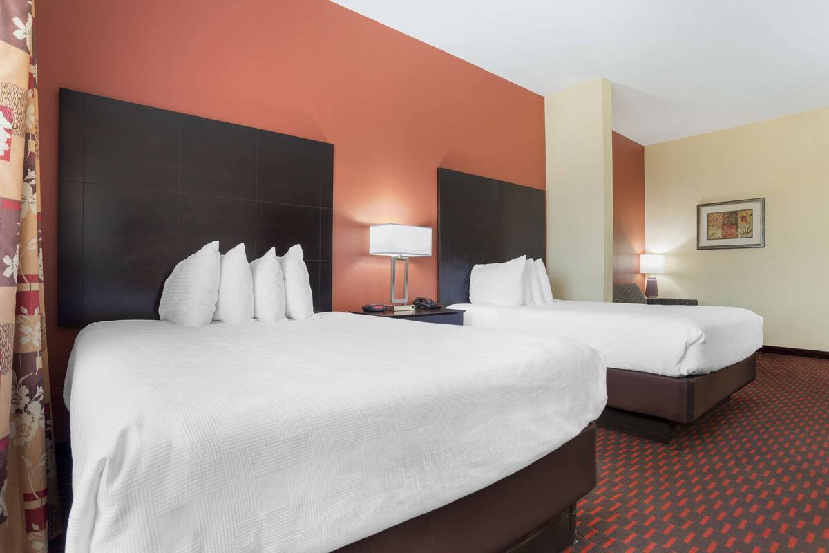 Ein Hotelzimmer mit zwei Betten, einem Nachttisch mit Lampe und einem gerahmten Bild an der Wand.
