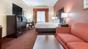 A hotel room with a bed, a desk with a computer, a TV, a sofa, and a lamp. - Best Western Plus Flowood Inn & Suites (Flowood)