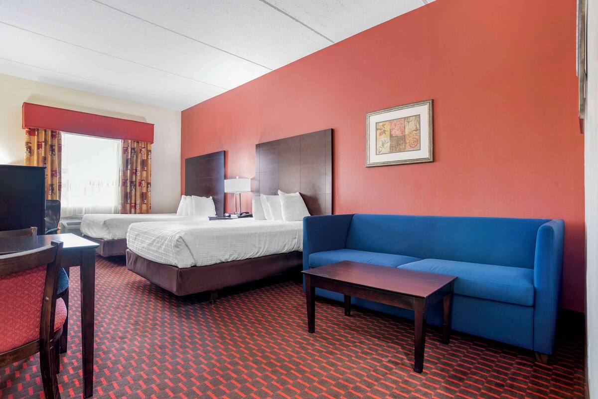Ein Hotelzimmer mit zwei Betten, einem blauen Sofa, einem Holztisch und einem Fernseher.