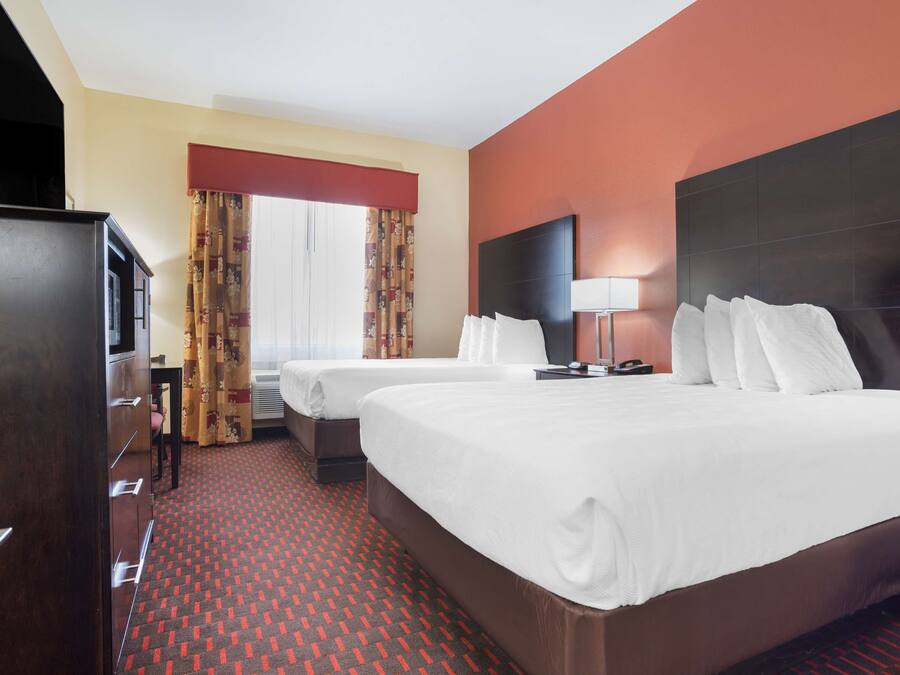 A hotel room with two beds, a desk, a TV, and a window with curtains.