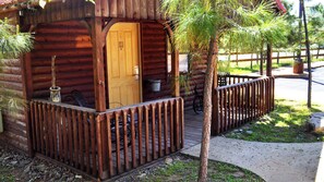 A wooden cabin with a wooden door, a porch with a railing, and a bicycle parked outside.