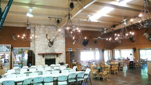 A spacious indoor area with multiple tables and chairs, a stone fireplace, and various ceiling lights.