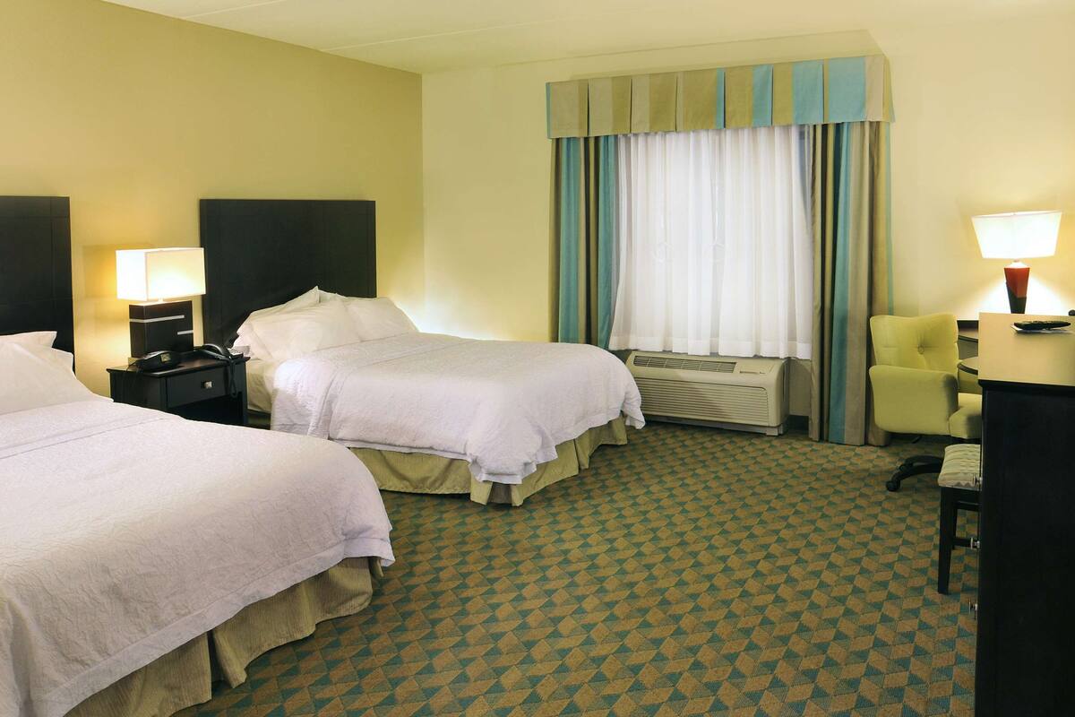 A hotel room with two beds, a television, a desk with a lamp, and a window with curtains.