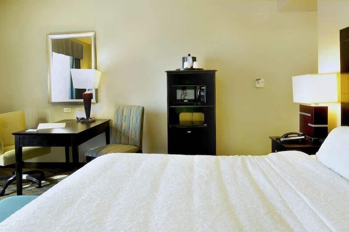 A hotel room with a bed, a desk, a chair, a TV, and a lamp.