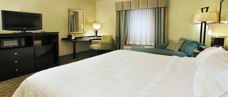 A hotel room with a large bed, a desk with a computer, a television, and a window with curtains.