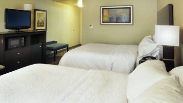Habitación de hotel con dos camas, un escritorio con televisor, microondas, una silla y un cuadro en la pared.