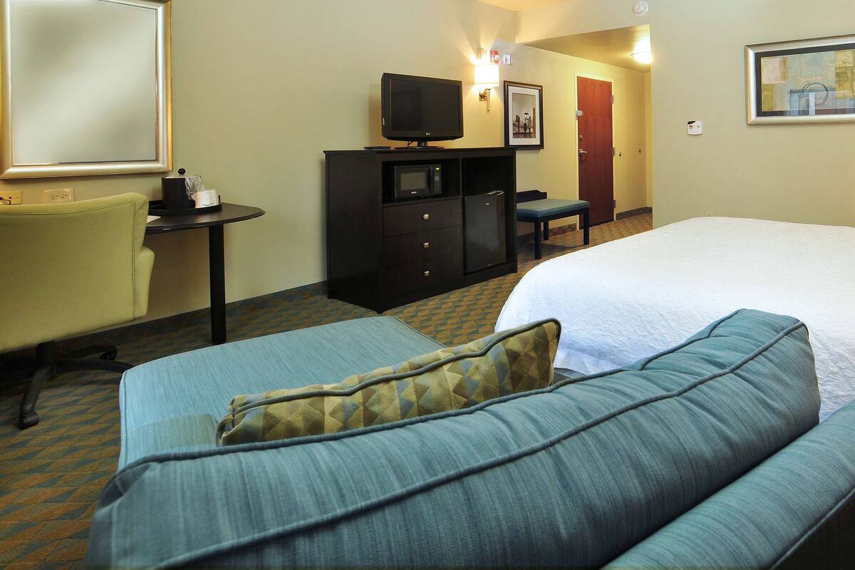 A hotel room with a bed, a sofa, a desk with a television, and a chair.