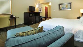 A hotel room with a bed, a sofa, a desk with a television, and a chair.