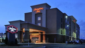 Un hôtel Hampton Inn doté d'une enseigne au néon bien visible, d'une entrée abritée et d'un parking.