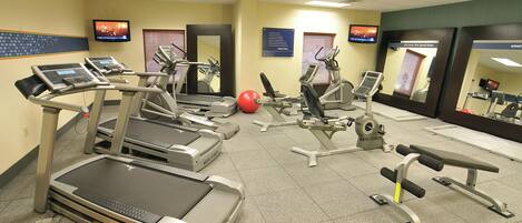 Gimnasio de hotel con cintas de correr, elípticas y una pelota de ejercicios roja.