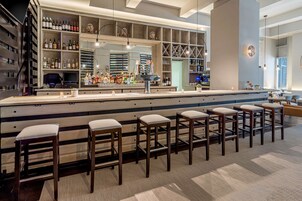 A bar area with a long counter, multiple stools, and shelves stocked with bottles.