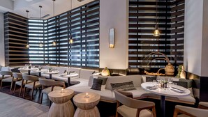 A modern restaurant with a contemporary interior, featuring a mix of seating options including round tables and sofas, with a decorative wall and pendant lighting.