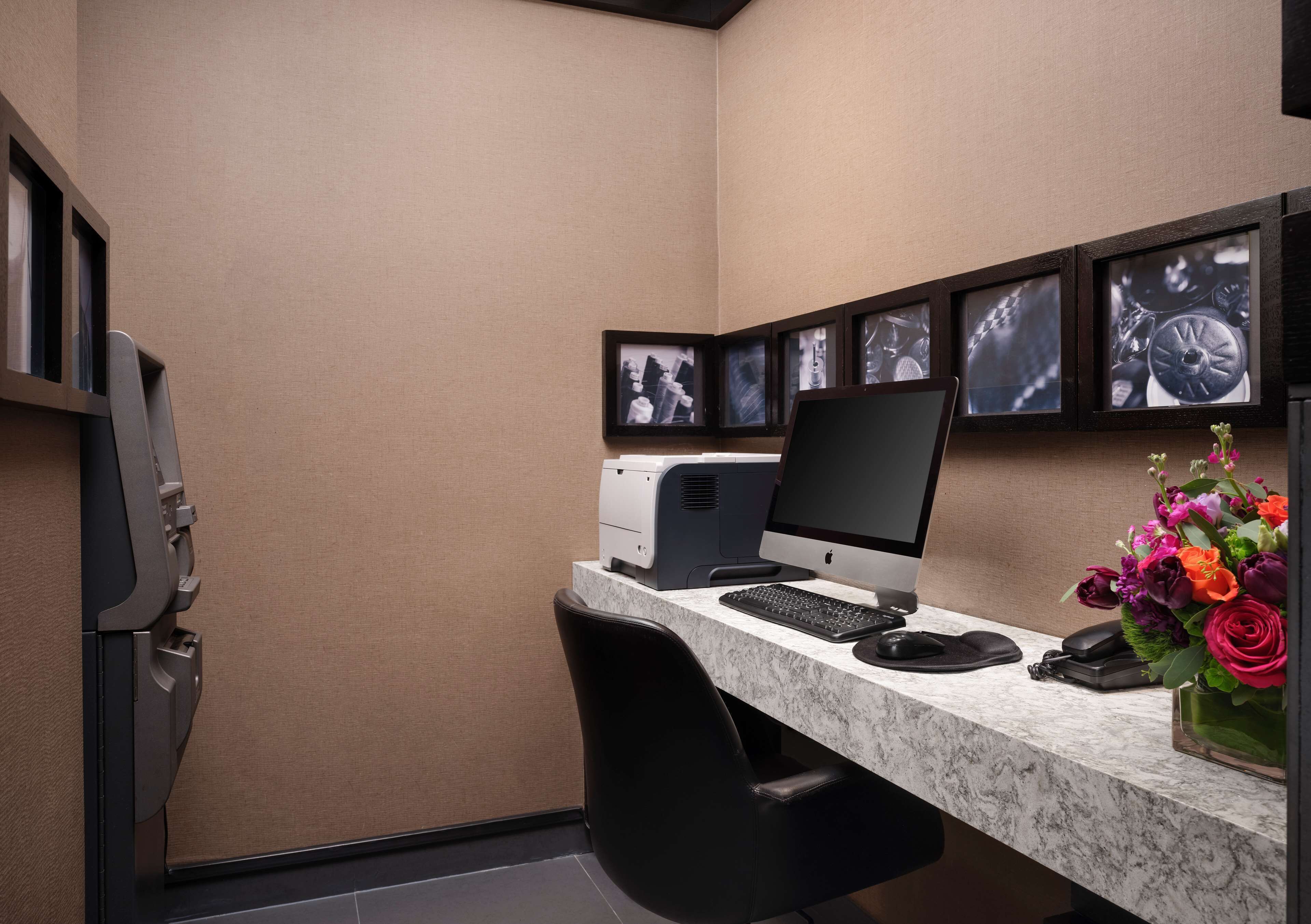 Een modern bureau met een computer, printer en toetsenbord. Een stoel staat ervoor, en rechts staat een vaas met bloemen.