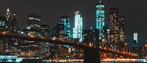 Un paisaje urbano nocturno con rascacielos iluminados y un puente destacado.