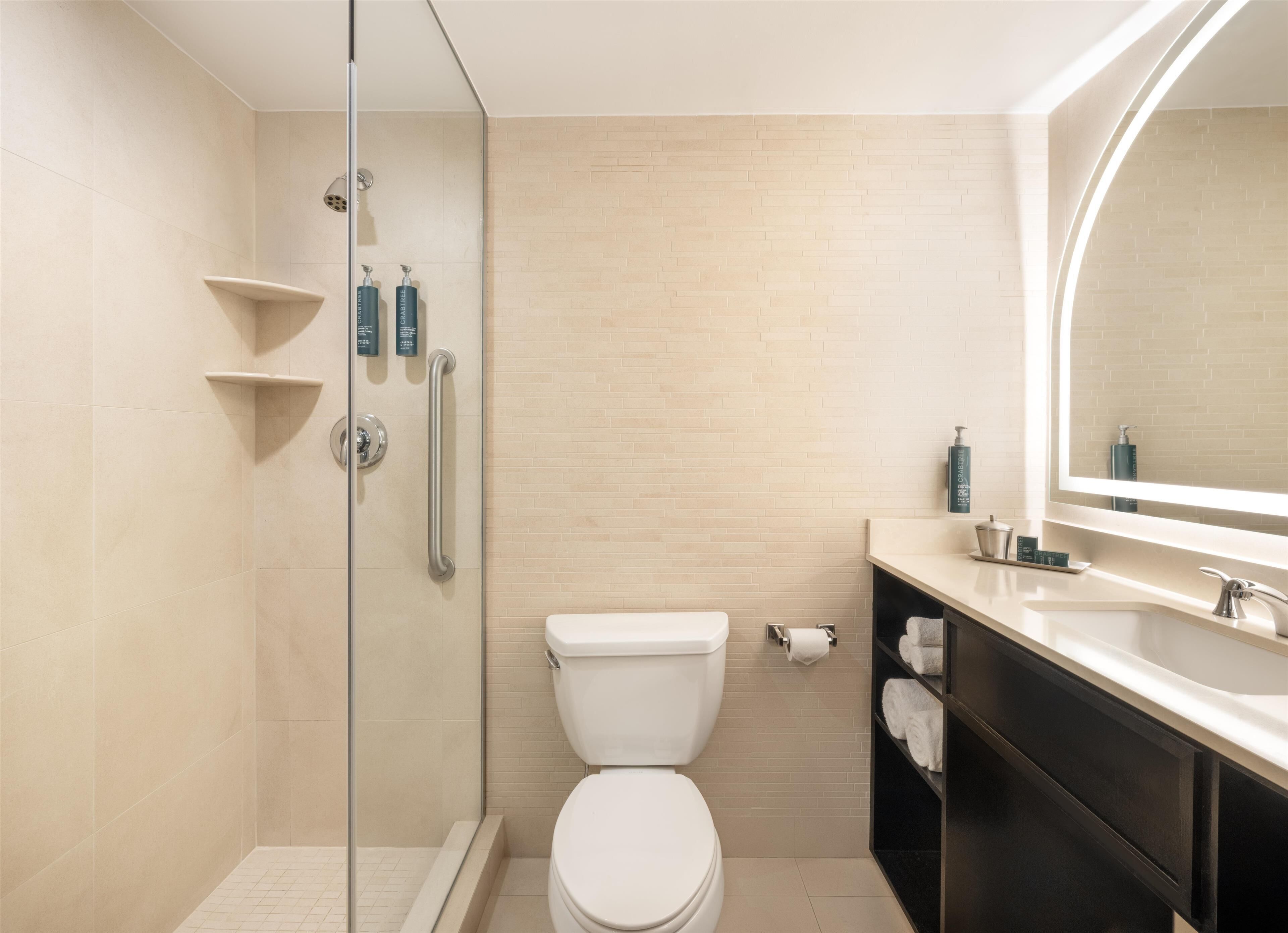 A modern bathroom with a glass-enclosed shower, a toilet, a sink with a mirror, and toiletries on the countertop.