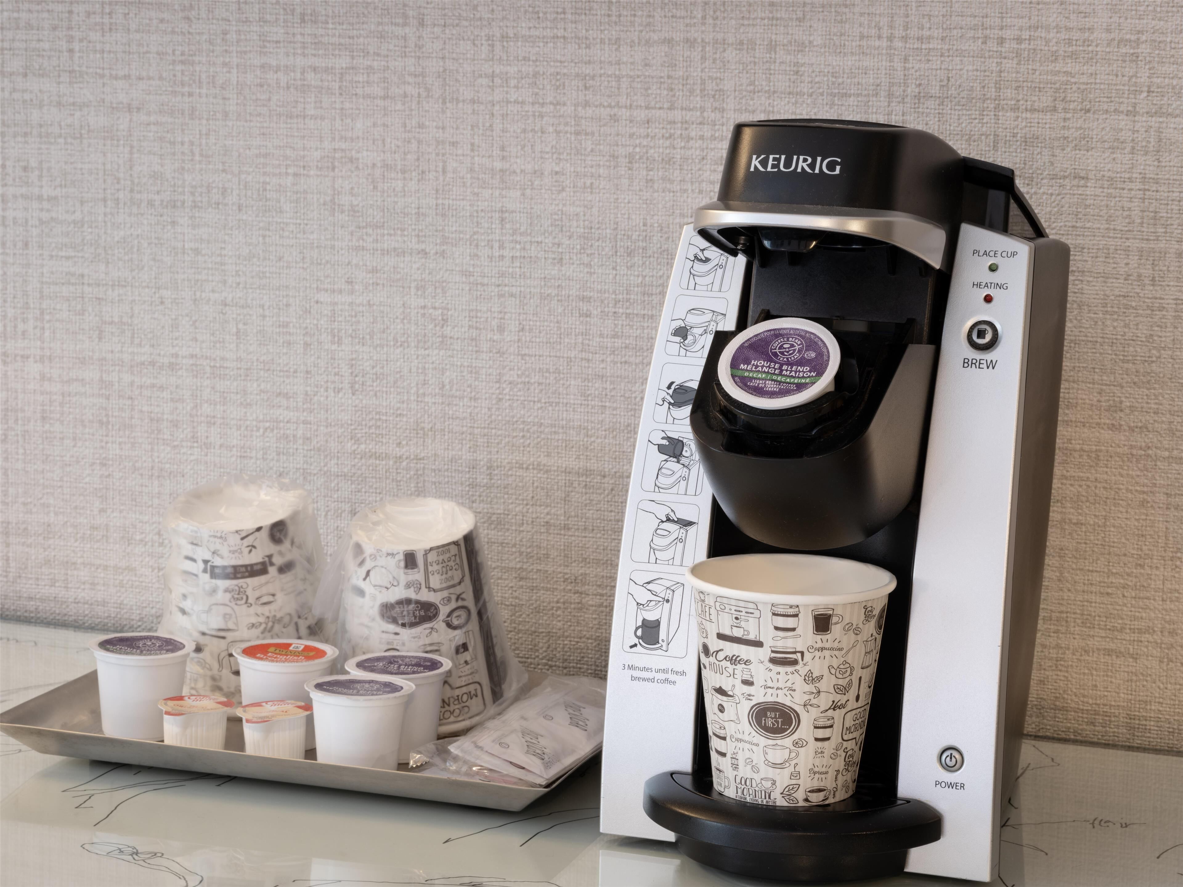 Una cafetera Keurig con una cápsula de café y un juego de vasos desechables.